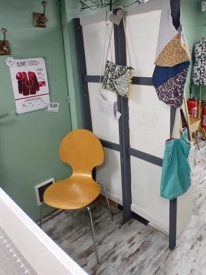 espace d'essayage avec porte manteaux sur la porte et chaise en bois avec paravent fait maison en bois et tissus.